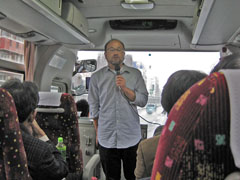 バスで出発。挨拶されているのは組織活性化委員会委員長・岩佐嘉彦会員です
